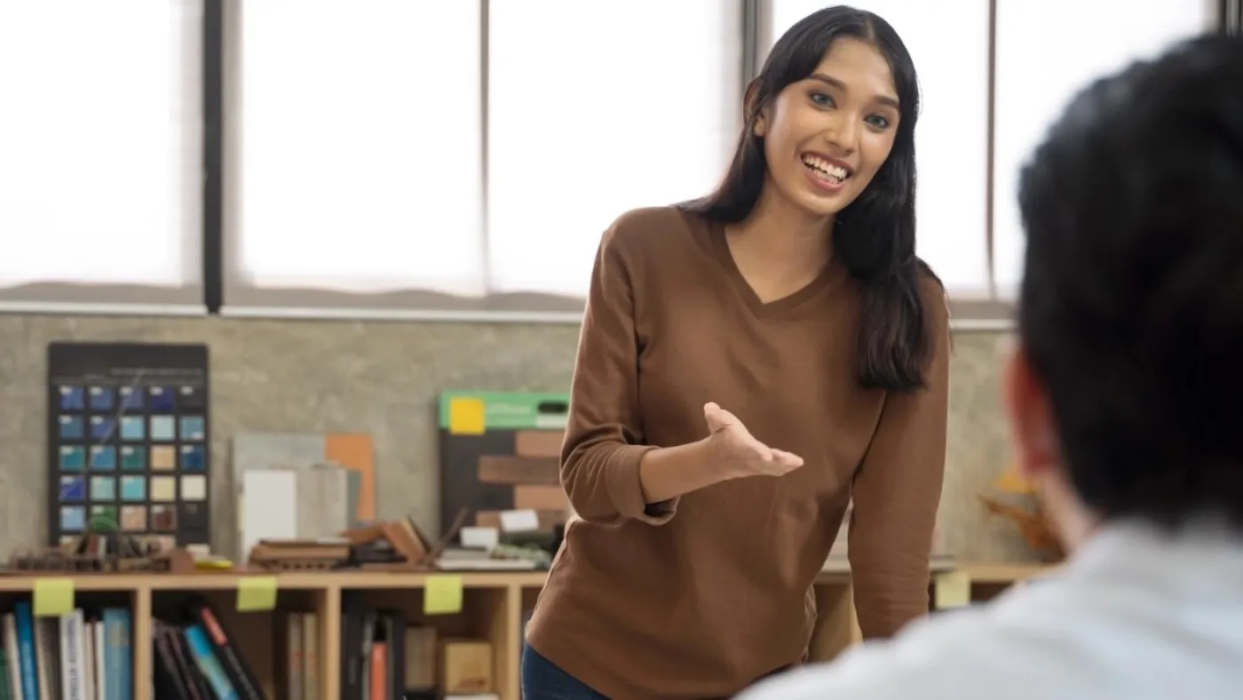 A young professional smiling and talking with a colleague in a bright studio.